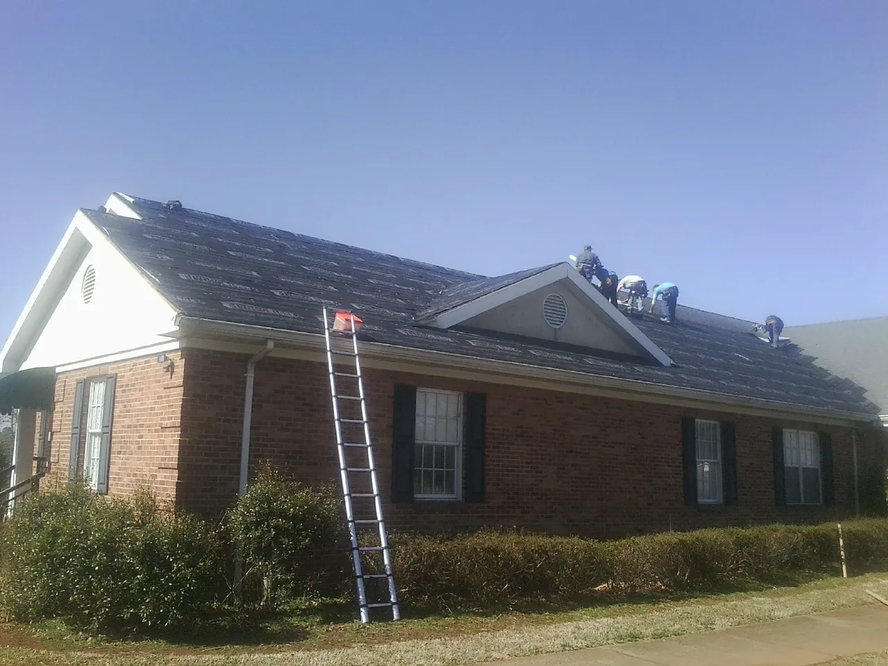 Crew tearing shingles off a brick ranch roof with a ladder set — Emergency Roof Repair work by our crew in Cohocton