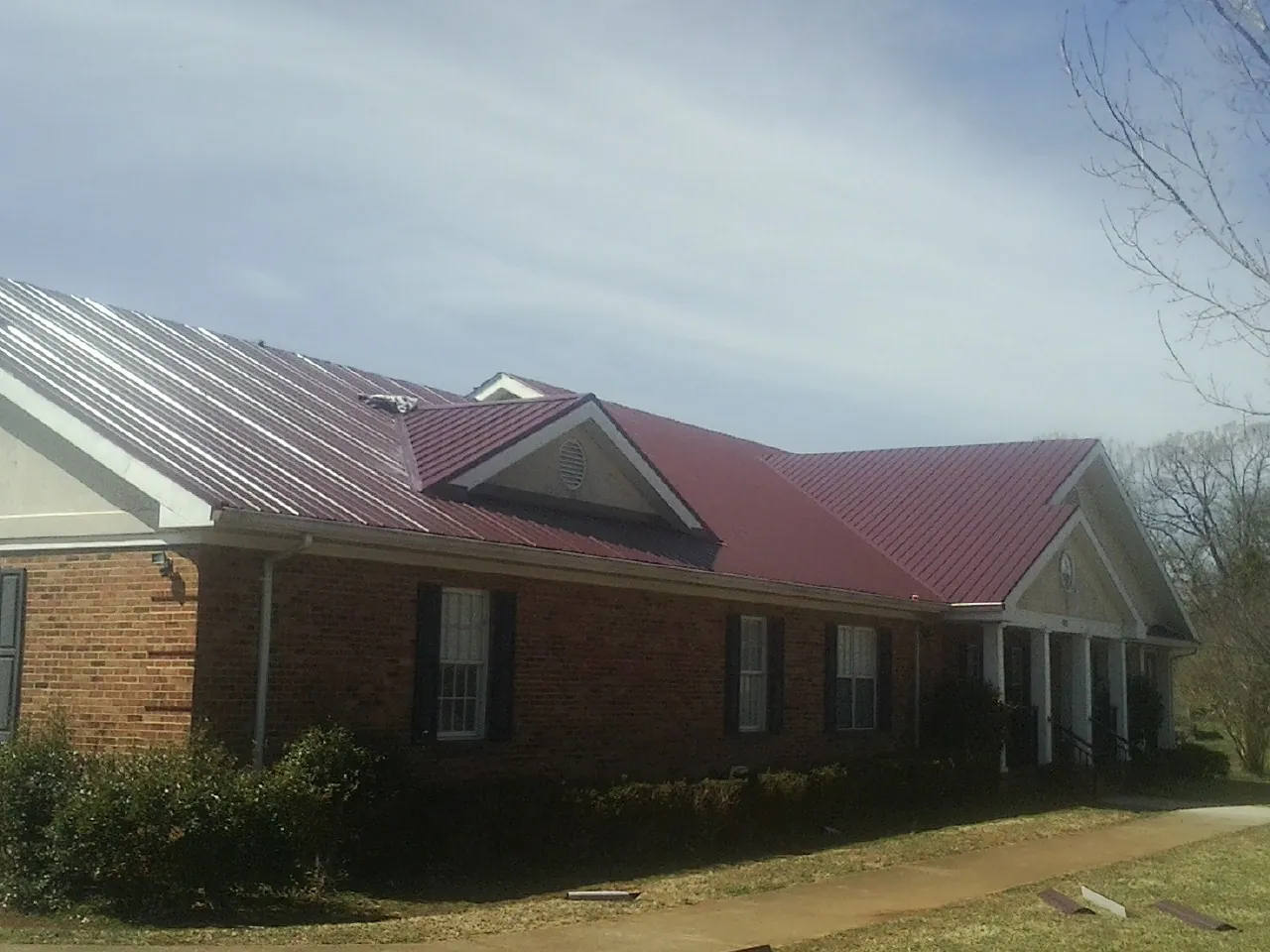 Red metal roof with gabled entries on a long brick building, from a Hail Damage Roof Repair job in Cohocton