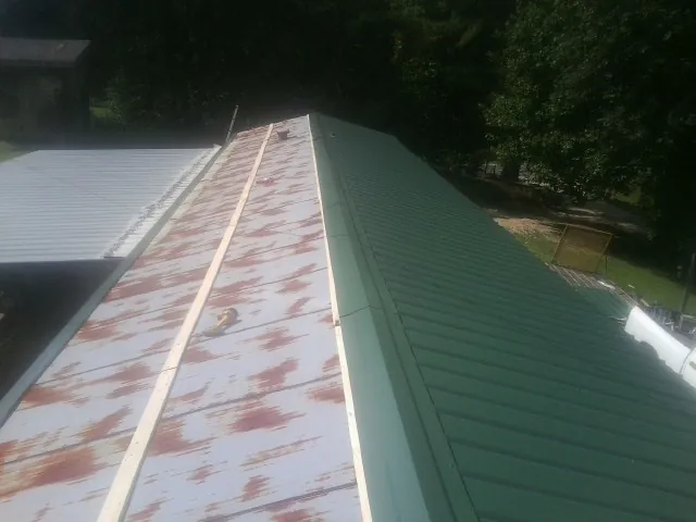 Old rusted panels beside newly installed green metal roofing — Wind Damage Roof Repair by Roofing Brothers in Cohocton