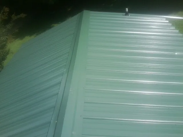 New green metal panels meeting at the ridge of a roof — Flat Roof Repair work by our crew in Cohocton