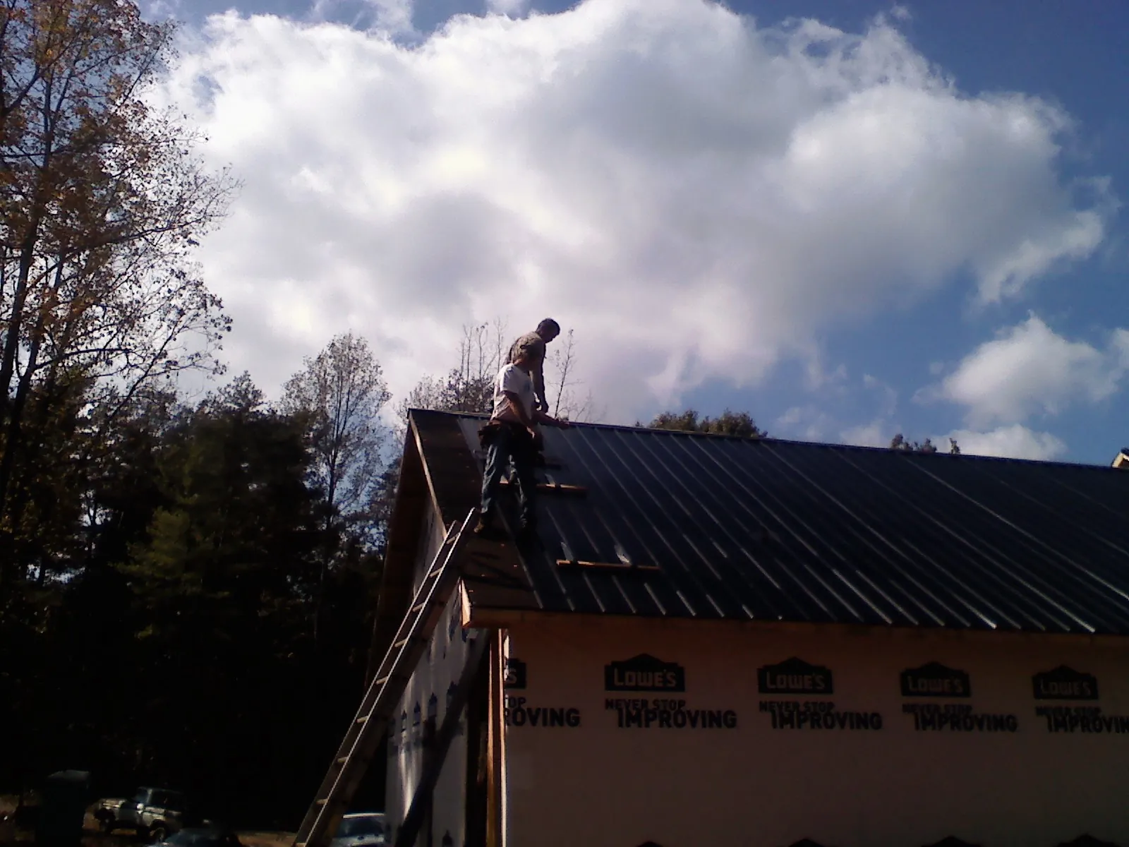 Roofer fastening dark metal panels high against a cloudy sky, from a Roof Inspection job in Cohocton