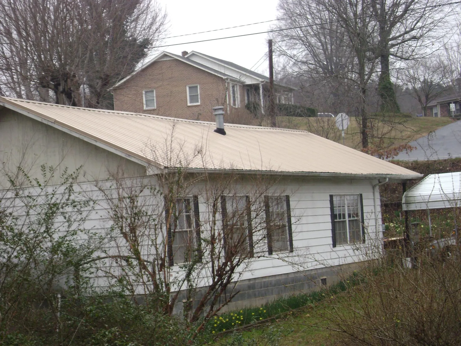 Tan metal roof on a white sided house set into a hillside — Commercial Roofing by Roofing Brothers in Cohocton