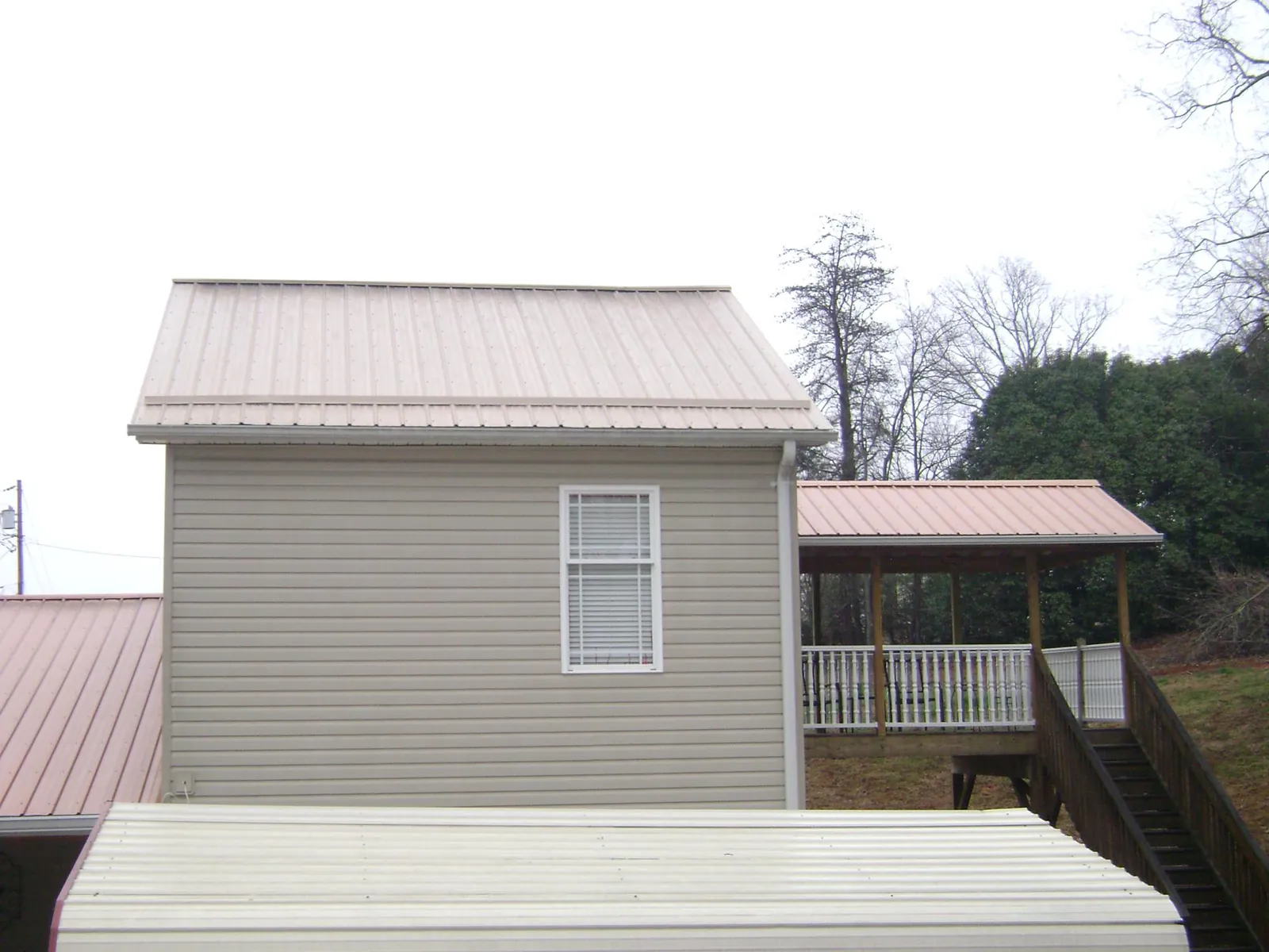 Tan metal roofs on a two story addition and attached porch, from a Roof Replacement job in Cohocton