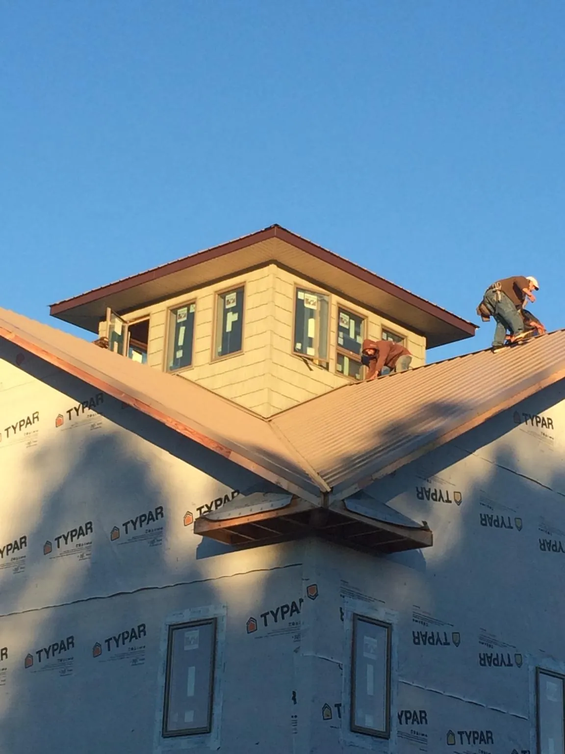 Roofers working around a rooftop cupola on a new metal roof at sunset — Roof Waterproofing in Cohocton by Roofing Brothers